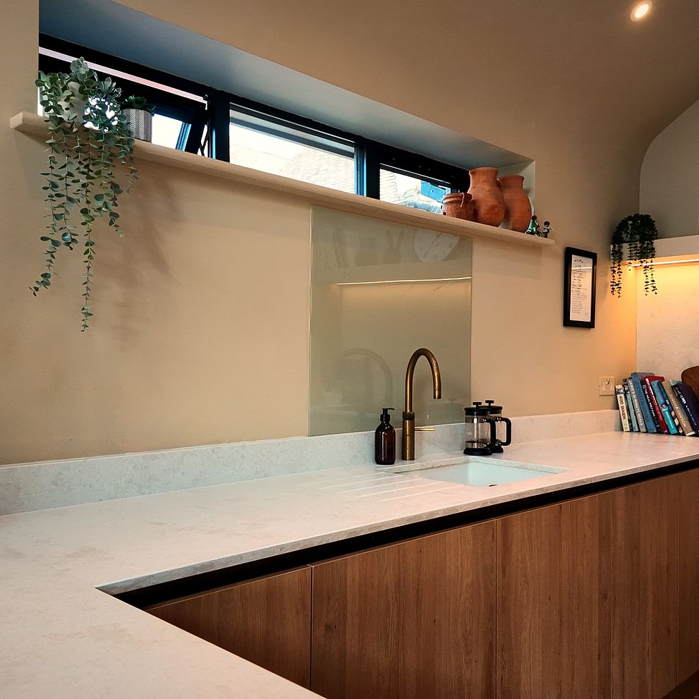 L-shaped kitchen with white worktops, high-level windows and shelf lighting